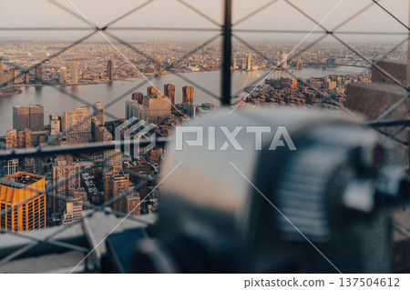 Visitors observe New York City skyline through a telescope at sunset 137504612