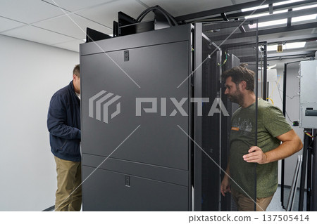 Two technicians installing and inspecting servers in a modern data center rack room for network infrastructure Two technicians installing and inspecting servers in a modern data center rack room for network infrastructure 137505414