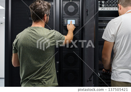 Two technicians working on server racks in a data center performing maintenance and system monitoring Two technicians working on server racks in a data center performing maintenance and system monitoring 137505421