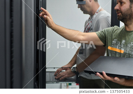IT technicians working in a data center server rack with laptop performing maintenance and troubleshooting IT technicians working in a data center server rack with laptop performing maintenance and troubleshooting 137505433