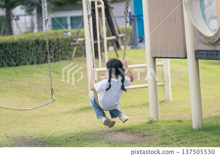 Joyful Child Swinging on Playground Swing in Sunny Park, Enjoying Outdoor Fun and Freedom in Simple White T-shirt and Blue Jeans Joyful Child Swinging on Playground Swing in Sunny Park, Enjoying Outdoor Fun and Freedom in Simple White T-shirt and Blue Jeans 137505530