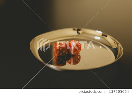 Two red dice on a reflective gold tray. Close-up still life with dark moody background and warm lighting. Concept of gambling, luck, risk, and fate. Cinematic aesthetic for business and leisure. 137505664