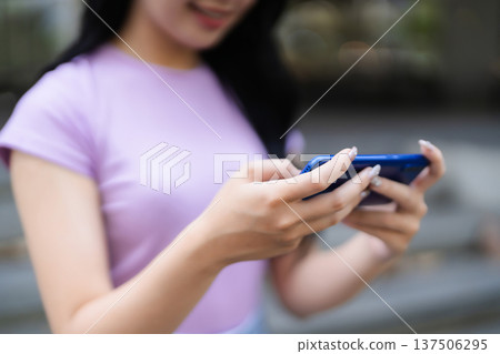 Asian adult woman hands hold modern blue smartphone playing mobile game or texting social media apps outdoor urban street digital lifestyle Asian adult woman hands hold modern blue smartphone playing mobile game or texting social media apps outdoor urban street digital lifestyle 137506295