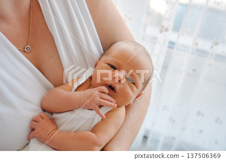 Newborn baby resting in mother's arms by a window Newborn baby resting in mother's arms by a window 137506369
