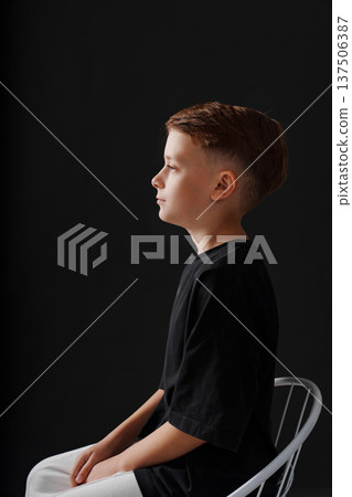 Young boy is sitting on a chair against a dark background Young boy is sitting on a chair against a dark background 137506387