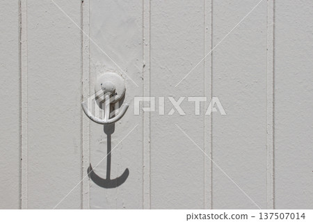 Old Metal Anchor Shaped Wall Hook on White Wooden Panel Background. Minimal Coastal Decor Detail. Nautical Interior Element. Rustic Marine Style, Simple Beach House Design Concept. Fitting room 137507014