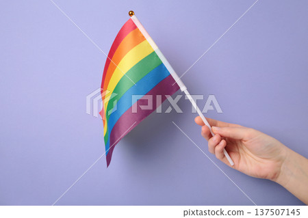 Hand holding rainbow flag on purple background. Hand holding rainbow flag on purple background. 137507145