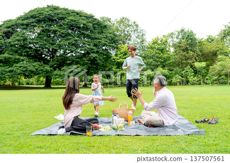 Little girl run to hug with her mother and follow by her father also grandfather sit on mat and cheer up the girl in public during happiness relax with family. 137507561