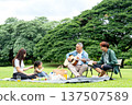 Asian little girl sit on mat to picnic during grandfather play the music using guitar and her father and mother also relax in public park with daylight. 137507589