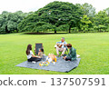 Wide shot of Asian little girl concentrate to draw and stay with father and mother also grandfather play the music using guitar and sit beside of them in public park with daylight. 137507591