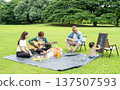Asian grandfather sit on chair and look at grandchild draw while young man play music using guitar in public park during they have holiday together with daylight. 137507593