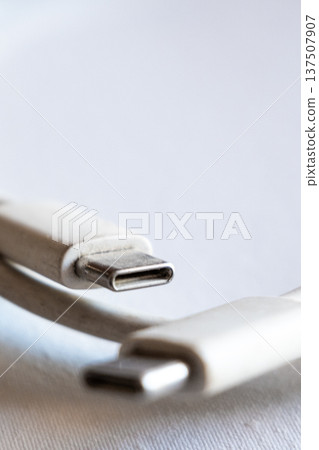 Close-up of a type-C cable with two connectors. The cable is white and flexible, lying on a light surface. Ideal for technology and electronics themes. Close-up of a type-C cable with two connectors. The cable is white and flexible, lying on a light surface. Ideal for technology and electronics themes. 137507907