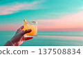 Sunset cocktail held above ocean, hand lifts chilled cocktail in frosted glass, pastel horizon frames cocktail as waves blur, refreshing beach sip invites slow evening relaxation, summer escape mood 137508834
