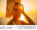 Smiling woman with towel at sunset, warm light kisses skin as sunset glow frames face, gentle breeze and beach background, sunset mood enhances relaxed wellness and carefree summer theme 137508835