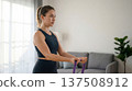 Focused woman trains with resistance band. Resistance band strength workout at home for new year fitness resolutions, healthy lifestyle, toning arms, body shaping, cozy daylight concept 137508912