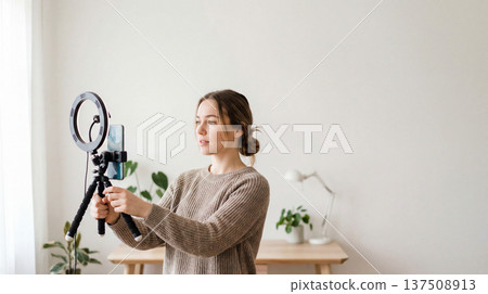 Woman films smartphone vlog with ringlight. Smartphone on tripod with ring light in bright home studio, smartphone video for blackfriday promo, cybermonday sale, minimal interior, copy space Woman films smartphone vlog with ringlight. Smartphone on tripod with ring light in bright home studio, smartphone video for blackfriday promo, cybermonday sale, minimal interior, copy space 137508913