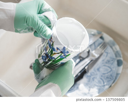 Man in green rubber gloves washes dishes 137509805