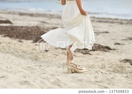 Bride in white dress and golden shoes on the beach Bride in white dress and golden shoes on the beach 137509833