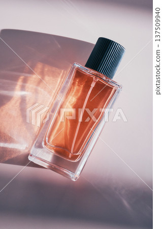 Luxury fragrance bottle creating elegant light patterns on subtle pink surface Luxury fragrance bottle creating elegant light patterns on subtle pink surface 137509940