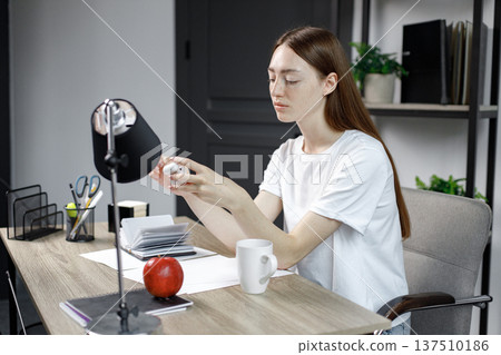 Cropped shot of bored girl wearing wireless earphones and studying at home. Beautiful girl at home learning. Woman has long red hair and white t-shirt. Cropped shot of bored girl wearing wireless earphones and studying at home. Beautiful girl at home learning. Woman has long red hair and white t-shirt. 137510186