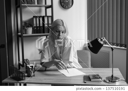 Man with make up on his face sitting in office and writing. Man wearing fashionable t-shirt and shirt. Man has long hair. Man with make up on his face sitting in office and writing. Man wearing fashionable t-shirt and shirt. Man has long hair. 137510191