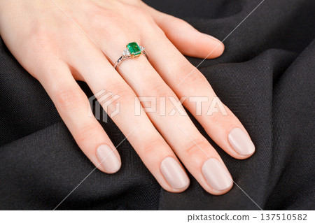 Beautiful female hand with gold ring with diamonds and emerald on gray background Beautiful female hand with gold ring with diamonds and emerald on gray background 137510582