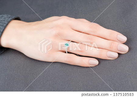 Beautiful female hand with gold ring with diamonds and emerald on gray background Beautiful female hand with gold ring with diamonds and emerald on gray background 137510583