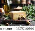 Block of cheese on rustic wooden board surrounded by fresh olives, olive oil, and herbs, creating a delicious culinary scene for gourmet food lovers 137510699