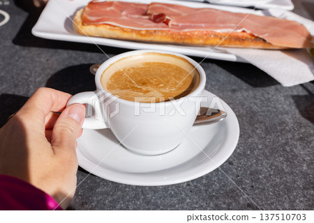 Woman drinking coffee with milk and eating tostada with ham in a cafe outside. 137510703
