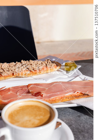 Coffee with milk and tostadas with tuna and ham. Spanish breakfast in a cafe outside. Coffee with milk and tostadas with tuna and ham. Spanish breakfast in a cafe outside. 137510706