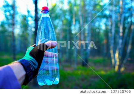 Water bottle in athlete's hand during a hike in woods. Water used for hydration in running sports Water bottle in athlete's hand during a hike in woods. Water used for hydration in running sports 137510766