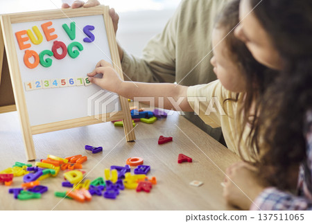 Parents guiding little daughter sorting colorful alphabet pieces during home play Parents guiding little daughter sorting colorful alphabet pieces during home play 137511065