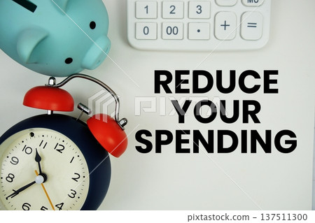 Reduce Your Spending text written notepad with calculator, piggy bank and alarm clock on white background 137511300