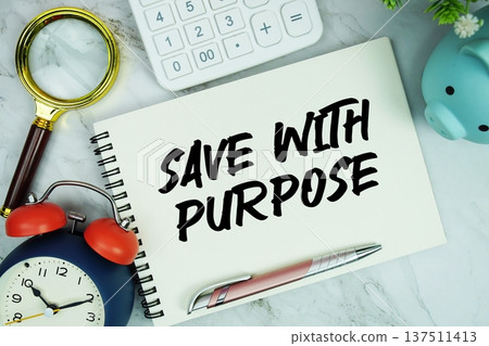 Save With Purpose text written on notepad with piggy bank, calculator, magnifying glass and alarm clock on marble background 137511413