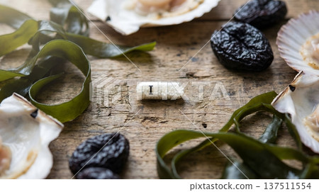 Iodine supplement capsule surrounded by natural food sources rich in iodine, scallops, seaweed, dried fruit, and nuts for thyroid health concepts 137511554
