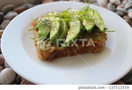 Healthy Nutrition Stock Photo. Plate With Toasted Bread Topped With Avocado and Fresh Peas Microgreens On A Sea Rocks   137511559