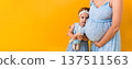 Motherhood, femininity, hot summer - croped banner pregnant unrecognizable woman mother in blue dress little happy girl baby sibling with teddy bear hugs care mom's big belly on yellow background 137511563