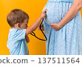 Motherhood, hot summer - croped portrait pregnant mother unrecognizable woman blue dress little boy son sibling treat pregnant mom role play stethoscope unborn brother mom tummy on yellow background 137511564