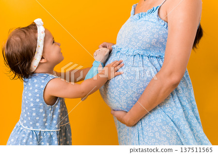 Motherhood, love, Childhood, hot summer - croped portrait pregnant mother unrecognizable woman blue dress little sibling girl sister hug touch mum big belly brother on yellow background copy space Motherhood, love, Childhood, hot summer - croped portrait pregnant mother unrecognizable woman blue dress little sibling girl sister hug touch mum big belly brother on yellow background copy space 137511565