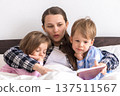 happy family. Close up loving mother lying with daughter son two kids pajamas in bed children reading interesting storybook, preschool smiling kid girl enjoy fairytale before go to sleep good pastime 137511567
