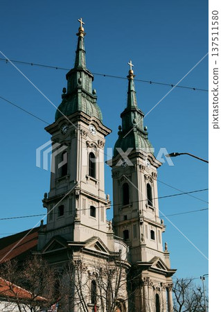 Twin towers of a historic Orthodox church rising above the city skyline in Pancevo, Serbia. Architectural landmark with crosses, clocks and baroque details under clear blue sky 137511580
