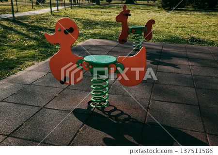 Bright orange spring rider playground toy standing on rubber safety surface. Outdoor play equipment designed for children recreation and fun Bright orange spring rider playground toy standing on rubber safety surface. Outdoor play equipment designed for children recreation and fun 137511586