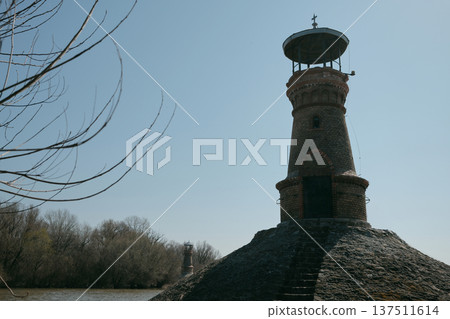 Historic lighthouse tower on the riverbank near Pancevo in Serbia with the Danube river landscape behind. Old navigation structure used as a landmark for river shipping and water transport Historic lighthouse tower on the riverbank near Pancevo in Serbia with the Danube river landscape behind. Old navigation structure used as a landmark for river shipping and water transport 137511614