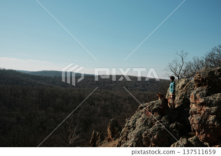 Female traveler standing on rocky cliff Orlove Stene in Fruska Gora, Serbia with German and Australian Shepherd dogs overlooking vast forest valley. Adventure and freedom concept in nature Female traveler standing on rocky cliff Orlove Stene in Fruska Gora, Serbia with German and Australian Shepherd dogs overlooking vast forest valley. Adventure and freedom concept in nature 137511659