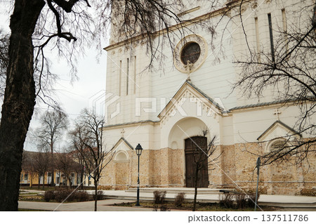 White church facade with arched entrance and stone wall in Sombor, Serbia. Historic European religious architecture and cultural heritage concept White church facade with arched entrance and stone wall in Sombor, Serbia. Historic European religious architecture and cultural heritage concept 137511786