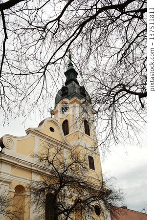 Church tower with clock rising above bare winter trees in Sombor, Serbia. Historic European architecture and cultural heritage travel concept Church tower with clock rising above bare winter trees in Sombor, Serbia. Historic European architecture and cultural heritage travel concept 137511811
