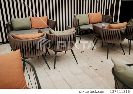 Warm outdoor cafe seating with empty chairs and soft cushions on a quiet terrace. Concept of calm urban lifestyle, hospitality design, comfort, slow living, and modern leisure space Warm outdoor cafe seating with empty chairs and soft cushions on a quiet terrace. Concept of calm urban lifestyle, hospitality design, comfort, slow living, and modern leisure space 137511816