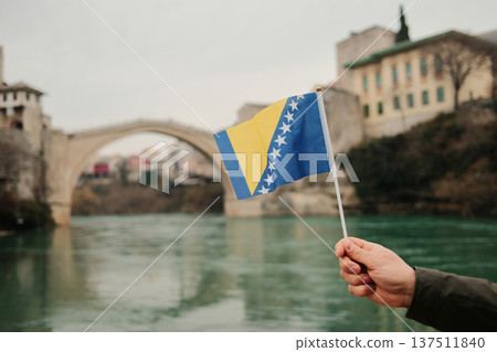 Hand holding Bosnia and Herzegovina flag in front of Stari Most bridge over Neretva river in Mostar. Symbol of national identity, history, travel and cultural heritage Hand holding Bosnia and Herzegovina flag in front of Stari Most bridge over Neretva river in Mostar. Symbol of national identity, history, travel and cultural heritage 137511840