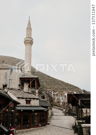 Stone street in Mostar old town leading past historic buildings and mosque minaret. Traditional Balkan urban scene with preserved architecture and calm atmosphere 137511847