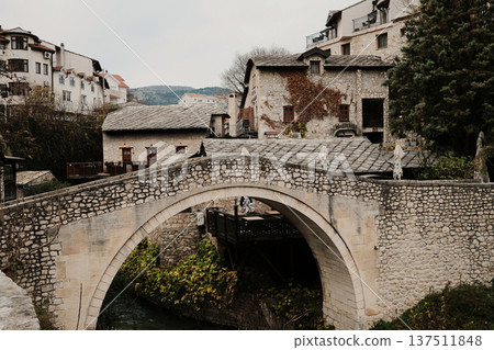 Kriva Cuprija stone bridge in Mostar crossing a shallow river, surrounded by historic houses and old town architecture. Medieval Balkan landmark reflecting cultural heritage and calm urban atmosphere Kriva Cuprija stone bridge in Mostar crossing a shallow river, surrounded by historic houses and old town architecture. Medieval Balkan landmark reflecting cultural heritage and calm urban atmosphere 137511848